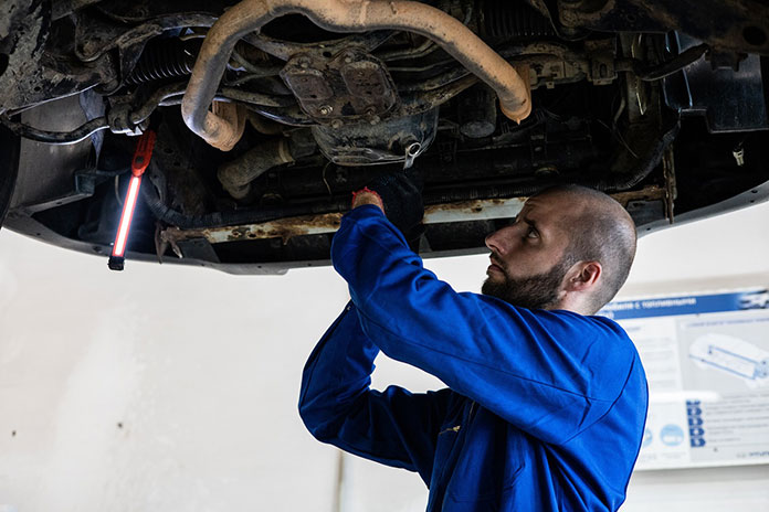 Mężczyzna naprawia auto na podnośniku w warsztacie samochodowym, w garażu umożliwiają to kanały samochodowe